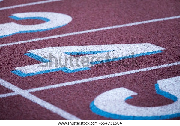Low macro close up on track and field crushed red\
rubber running surface divided into racing lanes labeled by painted\
number four with starting line marked by white stripe at athletic\
sport stadium