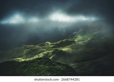 Low mist and storm clouds drift across the hills of Dovedale Valley, Lake District, with sunlight breaking through in a moody scene.