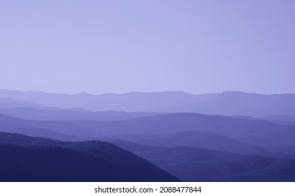 low mountains in mist toned in trendy Very Peri pantone color of the Year 2022. unspoilt hilly nature of haze away from man