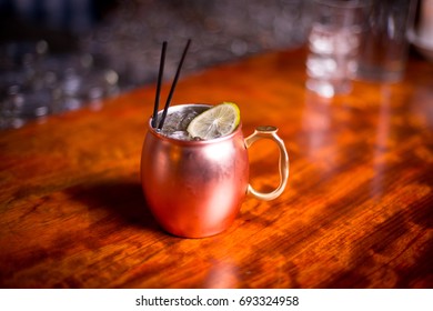 Low Overhead Perspective Close Up Of Poisonous Copper Mug With Bronze Handle Filled With Acidic Moscow Mule Alcoholic Beverage  With Ice Cubes And Sour Lime Slice Garnish Isolated On Counter Top Bar