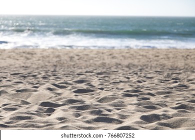 Low perspective seascape with focus on fine beach sand in the foreground and blurry waves and ocean water on the horizon in the background