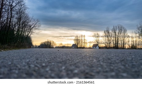 Low Perspective Vanishing Point Asphalt Road Between The Trees Of A Forest Under A Dramatic And Colorful Sunrise Or Sunset Sky. High Quality Photo