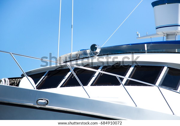 Low perspective view of front bow and navigation\
bridge with communication equipment of expensive mega yacht with\
black tinted windows and chrome metal railings on white fiber glass\
hull with blue sky