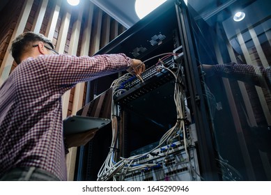 Low point view photo with relfections in the server room a technician/ It engineer/ hold the notebook and adjust the internet  connecting or fix the server error.