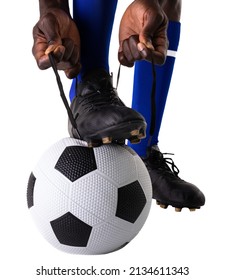 Low section of african american male soccer player tying shoelace on ball against white background. unaltered, sport, competition and match concept.