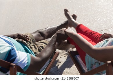 Low section of african american senior couple holding hands sitting on chairs at beach. unaltered, love, togetherness, lifestyle, enjoyment and holiday concept.
