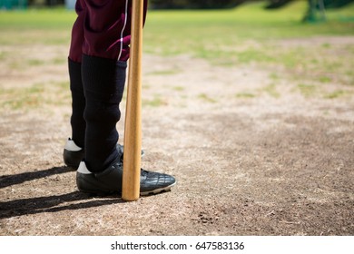 Low section of baseball player holding bat while standing on field during sunny day