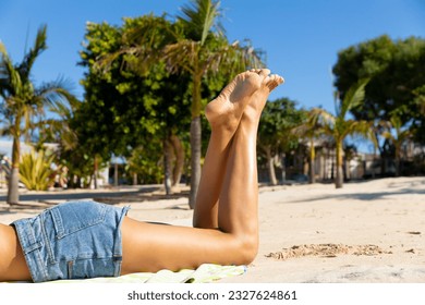 Low section of biracial woman in denim shorts lying on towel on sunny beach, copy space. Sunbathing, summer, free time, relaxation, lifestyle and vacation. - Powered by Shutterstock
