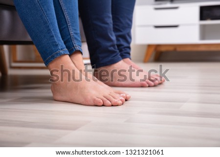 Low Section Of Couple's Feet On Floor In Living Room