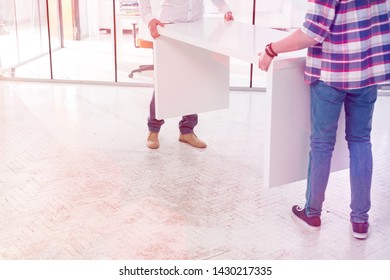 Low Section Of Creative Colleagues Carrying Desk While Setting Up Office