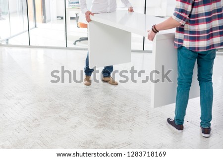 Low section of creative colleagues carrying desk while setting up office