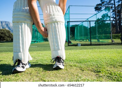 Low section of cricket player tying kneedpad while standing on grassy field