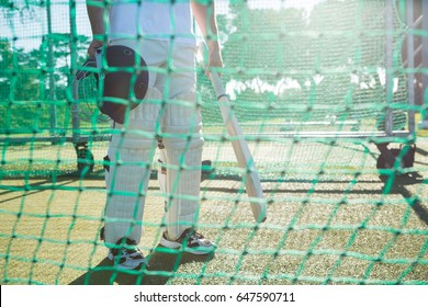 Low section of crickter standing by net at field on sunny day