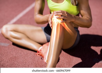 Low section of female athlete suffering from knee pain while sitting on track during sunny day - Powered by Shutterstock