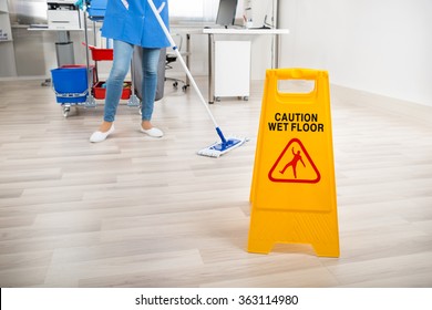 Low section of female janitor mopping floor by yellow wet caution sign in office - Shutterstock ID 363114980