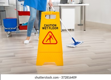 Low Section Of Female Janitor Mopping Floor By Yellow Wet Caution Sign In Office