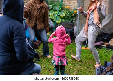 Low Section Of Females Dancing On Lawn While Girl In Pink Hoodie Standing And Looking At Them On Lawn. During Event At World And Spoken Word Festival