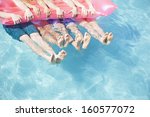 Low section of four friends in pool holding onto inflatable raft with feet sticking out of water