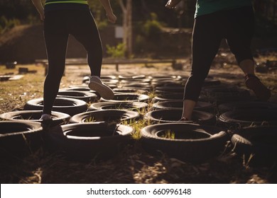 Low section of friends running over tyres during obstacle course in boot camp