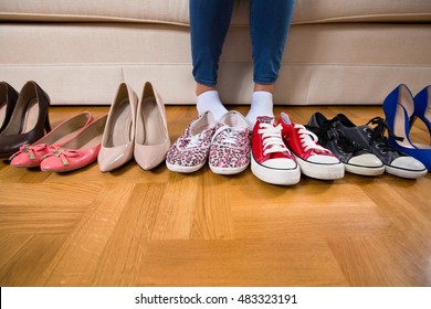 Low section of a girl sitting on the sofa with a lot of shoes in front of her, choosing what to wear, sneakers or high heels. - Powered by Shutterstock