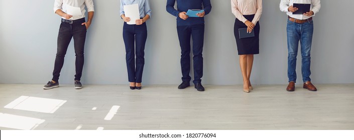 Low section of group of male and female candidates waiting in line for job interview. Company workers with office documents standing in queue to sign their papers. Website banner, header