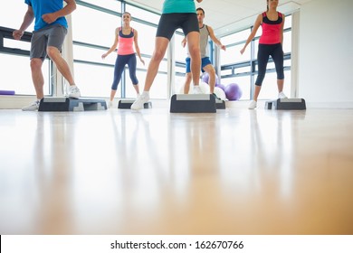 Low section of instructor with fitness class performing step aerobics exercise in gym - Powered by Shutterstock