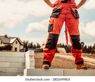 Low Section Legs Of Construction Worker Wearing Workwear Trousers And Brown Leather Work Boots Standing On Airbrick Wall.