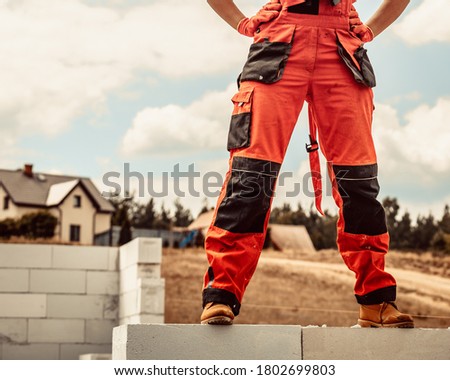 Low section legs of construction worker wearing workwear trousers and brown leather work boots standing on airbrick wall.
