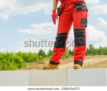 Low section legs of construction worker wearing workwear trousers and brown leather work boots standing on airbrick wall.