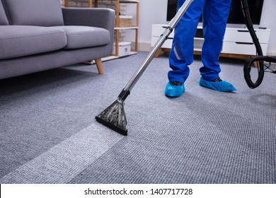 Low Section Of A Male Janitor Cleaning Carpet With Vacuum Cleaning In The Living Room