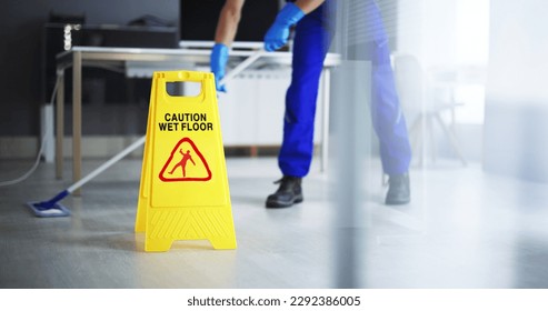 Low Section Of Male Janitor Cleaning Floor With Caution Wet Floor Sign In Office