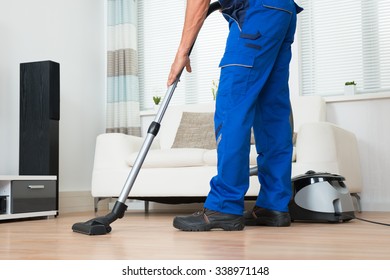 Low section of male janitor cleaning floor with vacuum cleaner in living room