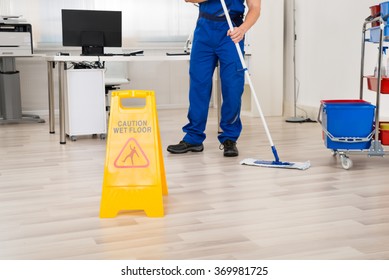 Low section of male janitor cleaning floor with mop in office
