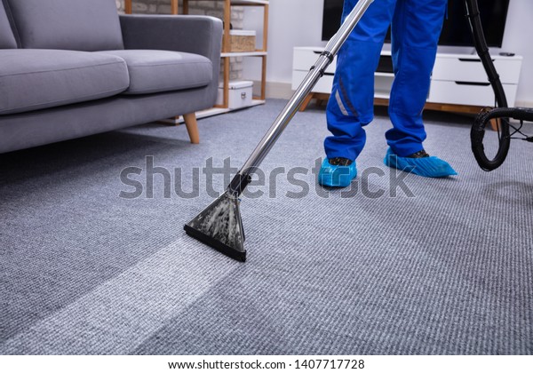 Low Section Of A Male Janitor Cleaning\
Carpet With Vacuum Cleaning In The Living\
Room