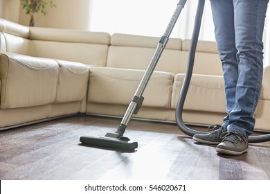 Low Section Of Man Cleaning Hardwood Floor With Vacuum Cleaner