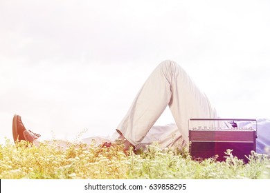 Low section of man lying by vintage radio on grass against clear sky