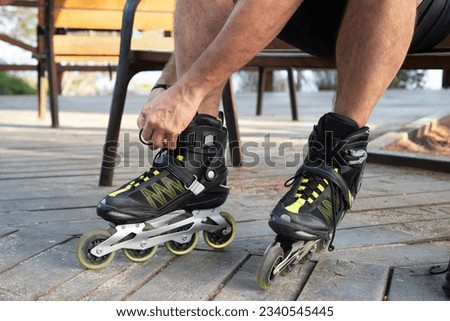 Low section of man sitting on a wooden bench while is tying rollerblades.