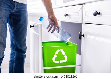 Low Section Of Man Throwing Empty Plastic Bottle In Recycling Bin In The Kitchen