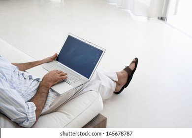Unterer Teil von Mann mittleren Alters mit Laptop auf Sofa im Wohnzimmer