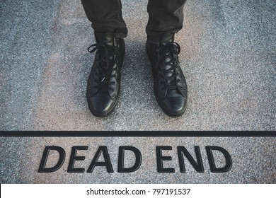 Low section of a person standing with a "dead end" written on the ground