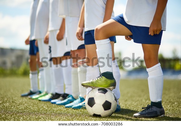 Low\
section portrait of junior football team : legs of boys standing in\
row with captain stepping on ball in\
foreground