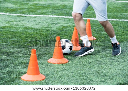 Low section portrait of unrecognizable muscular man leading ball between orange cones during football practice, copy space