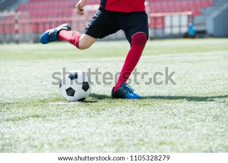 Low section portrait of unrecognizable teenage boy kicking ball playing football on stadium during practice, copy space