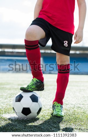Low section portrait of unrecognizable teenage boy wearing red uniform standing on football field and stepping on ball