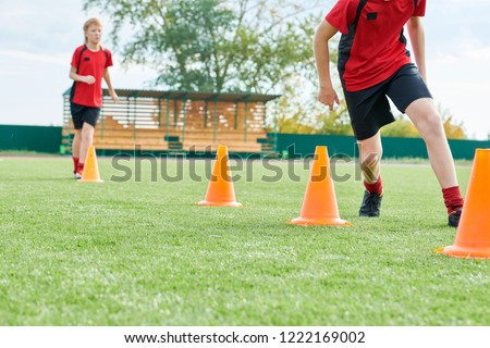 Low section portrait of unrecognizable teenage boys running between orange cones during football practice outdoors, copy space