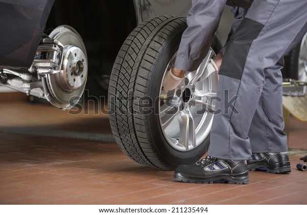 Low\
section of repairman fixing car\'s tire in repair\
shop