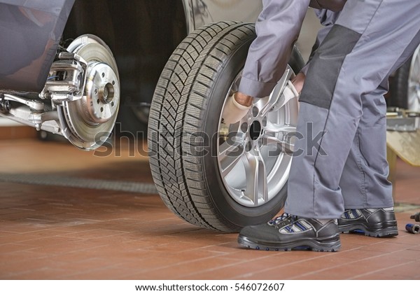 Low\
section of repairman fixing car\'s tire in repair\
shop