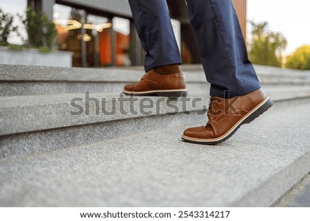 Low section of senior male entrepreneur in brown leather shoes moving up on staircase in modern city