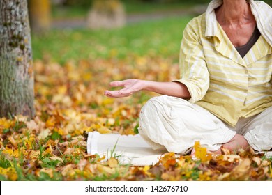 Low section of senior woman meditating while sitting in lotus position at park