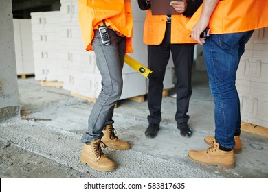 Low section shot of legs of two construction workers wearing jeans and brown leather work boots standing with man in suit on concrete floor